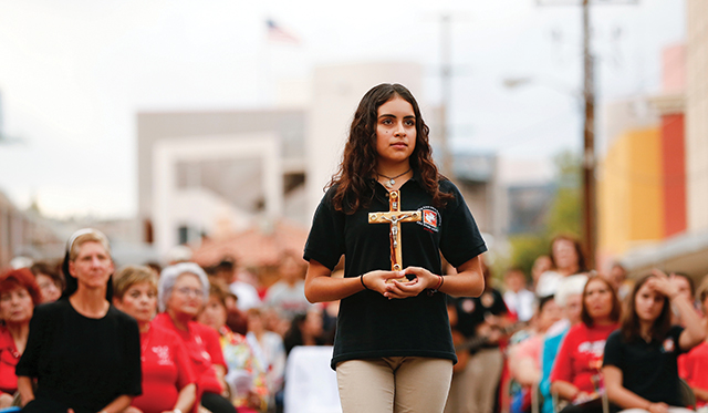 Vision 2024 Feister 10 Mercy meets at the border During the Offertory procession at a border Mass in Nogales, a girl carries a cross to remember the migrants who have died in the desert.